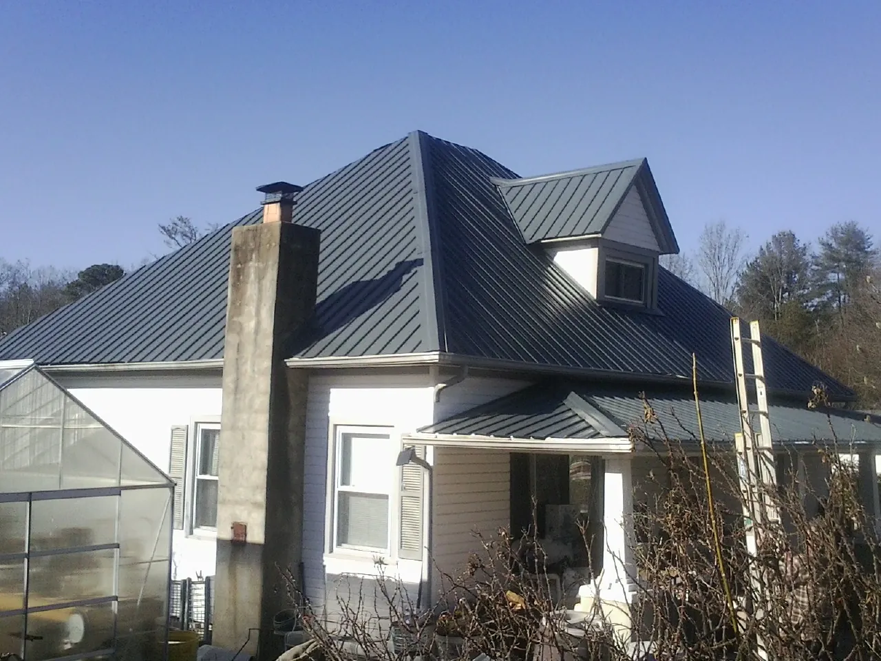 Dark blue standing seam metal roof on a white farmhouse with dormer — Slate & Tile Roof Repair by Roofing Brothers in Jones Mills