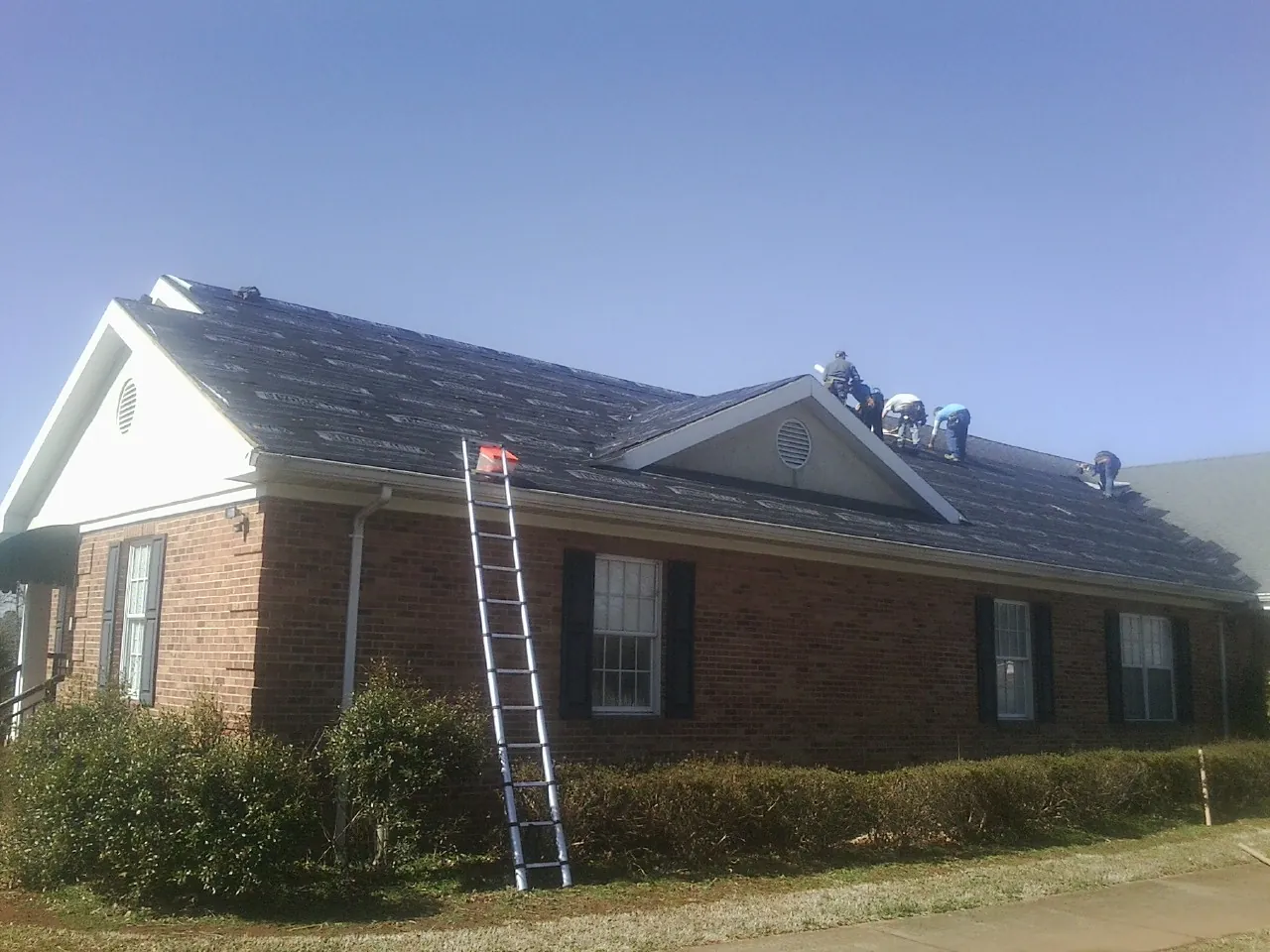 Crew tearing shingles off a brick ranch roof with a ladder set — Metal Roof Repair work by our crew in Jones Mills