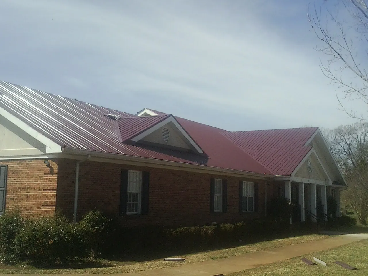 Red metal roof with gabled entries on a long brick building, from a Hail Damage Roof Repair job in Jones Mills