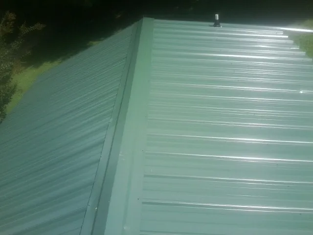 New green metal panels meeting at the ridge of a roof — Flat Roof Repair work by our crew in Jones Mills