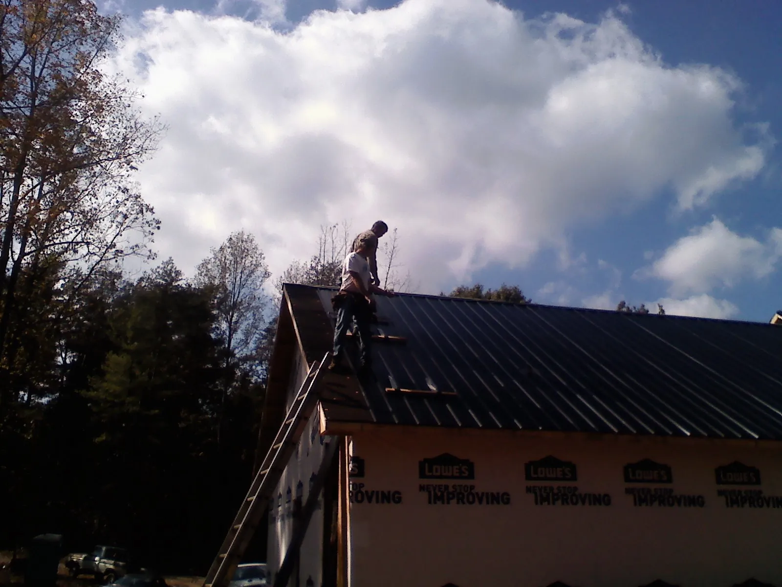 Roofer fastening dark metal panels high against a cloudy sky, from a Roof Inspection job in Jones Mills
