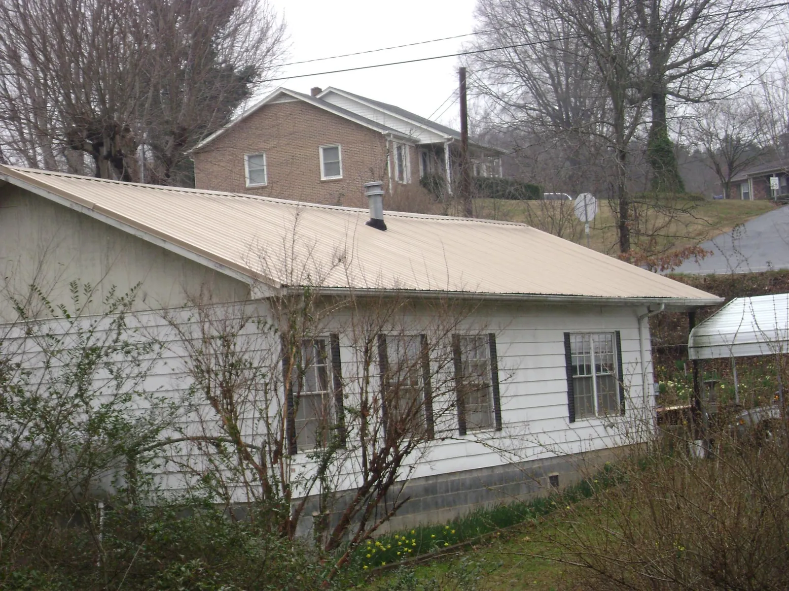 Tan metal roof on a white sided house set into a hillside — Commercial Roofing by Roofing Brothers in Jones Mills