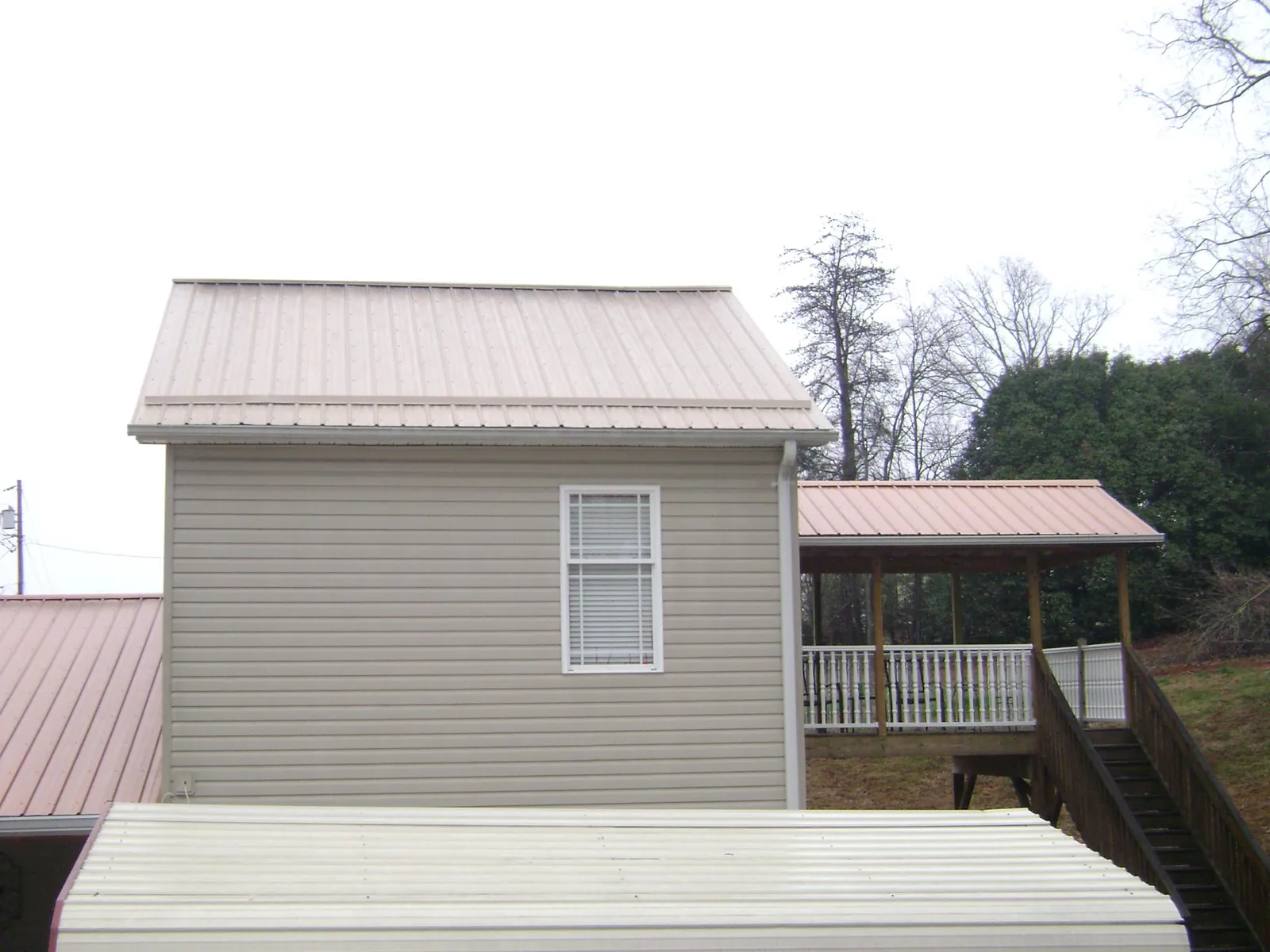 Tan metal roofs on a two story addition and attached porch, from a Roof Replacement job in Jones Mills